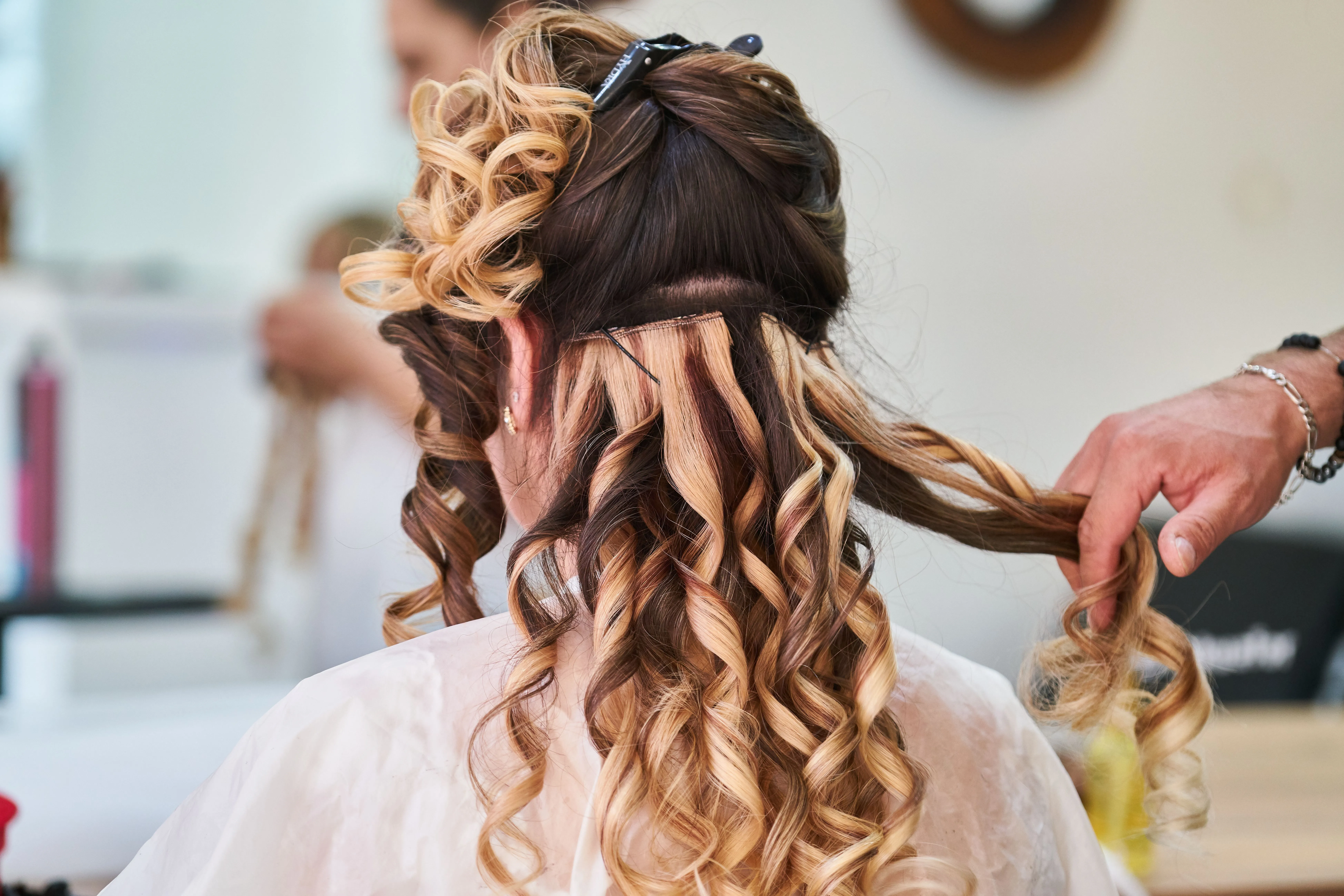 Stylist fitting a colour-matched weft into long curled hair - hair extensions at Characters Hair Randwick