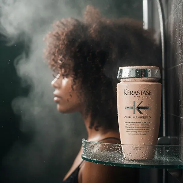 Kérastase Curl Manifesto hydrating shampoo in the shower beside a client with natural curls