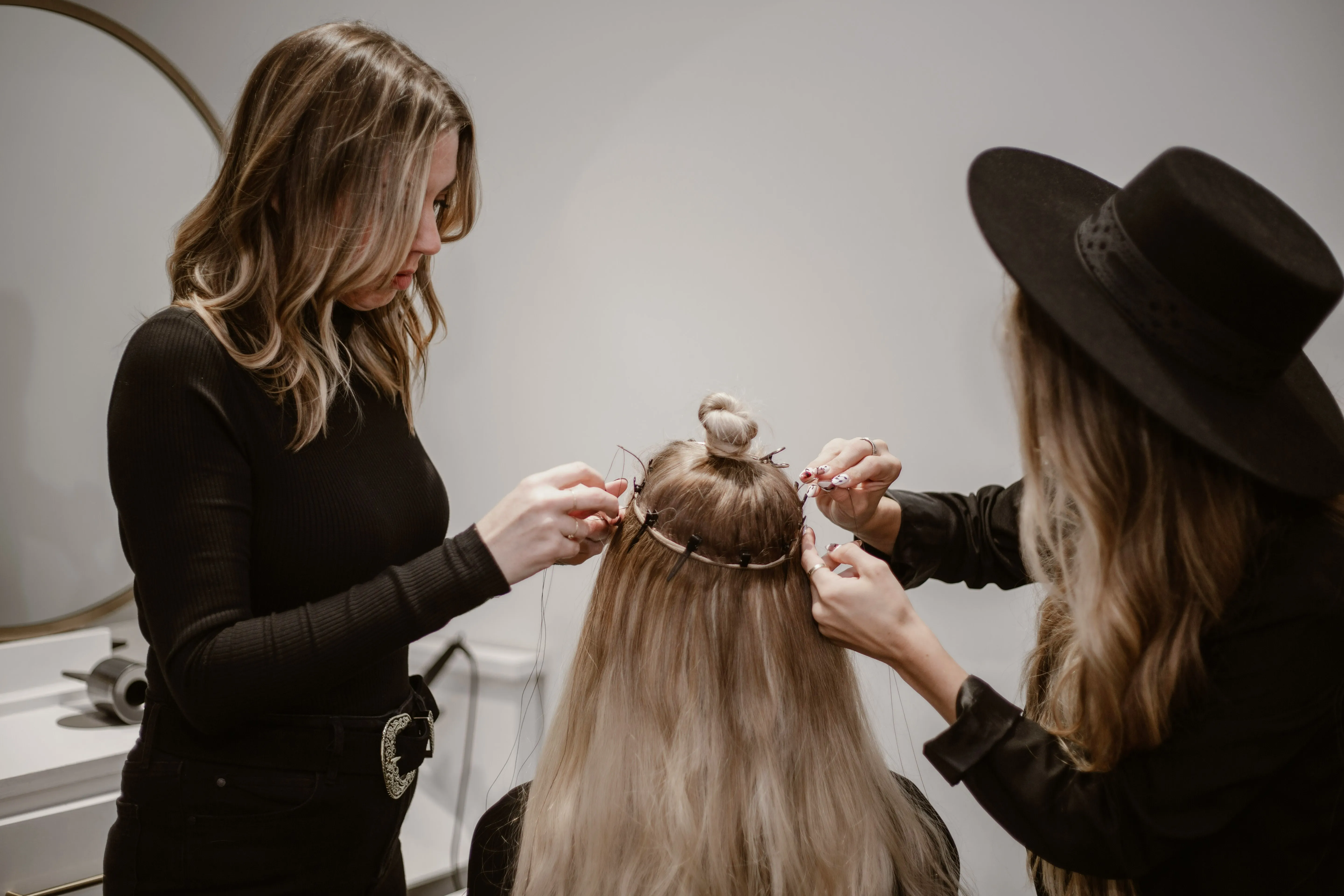 Stylists sewing a hand-tied weft into a blonde client’s hair at Characters Hair, Randwick
